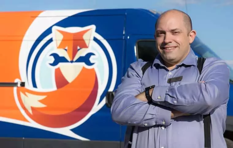 A man in a blue shirt stands with arms crossed in front of a van featuring a fox logo holding two wrenches.