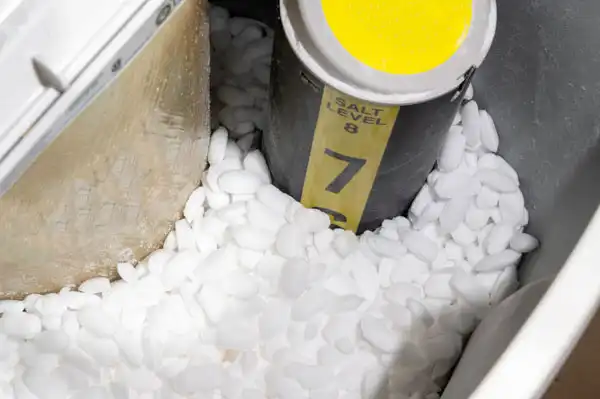 Close-up of a water softener brine tank, salt pellets surrounding a yellow salt level indicator marked with 7 and 8—a helpful view for anyone considering water softener repair.