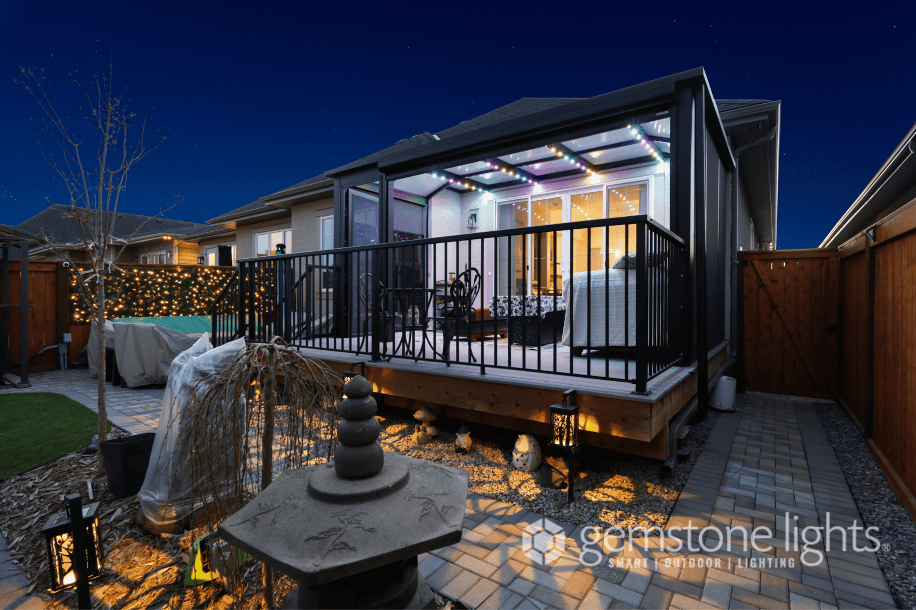 A covered backyard patio with LED ceiling lights, black railing, outdoor furniture, and paver walkway is showcased at night—offering a glimpse into the inviting spaces featured in our about us story.