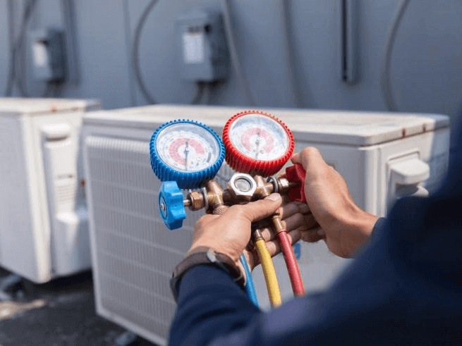 A technician skillfully uses a manifold gauge set with red and blue dials to perform AC repairs on outdoor units.