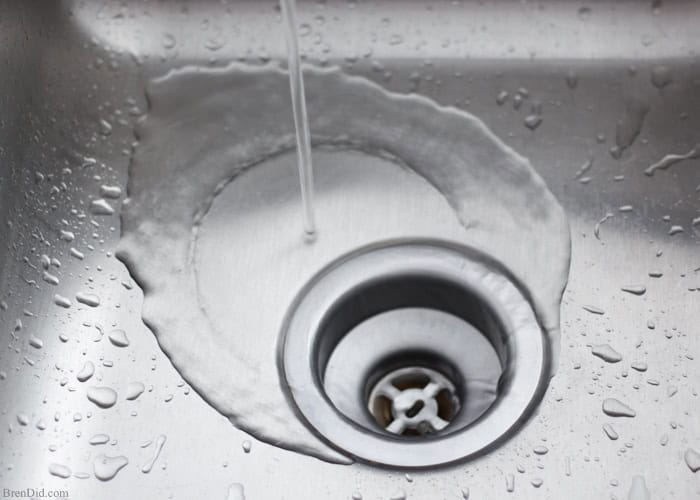 Water gently flows into a stainless steel sink, droplets scattering around. Be mindful of plumbing issues, as they can lead to unexpected drain clogs if not addressed promptly.