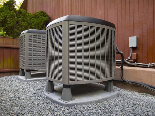 Two outdoor air conditioning units sit on a gravel surface next to a brown building, ready to tackle common heating problems often faced during the brisk Florida winter.