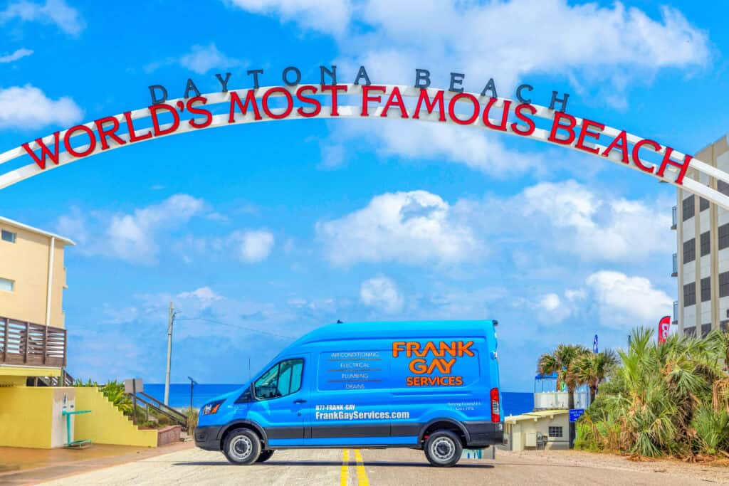 A blue service van, emblazoned with a logo promoting exciting career opportunities, is parked under the "Daytona Beach World's Most Famous Beach" archway on a sunny day.