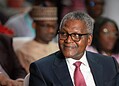 Senior professional man wearing glasses at formal event, listening attentively with diverse audience in background.