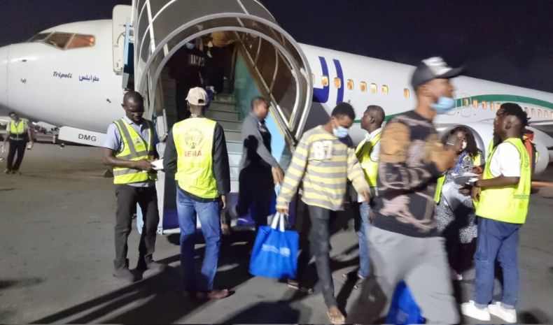 Boarding passengers onto a small commercial jet at night, with crew and travelers wearing safety vests and masks, preparing for departure at an airport.