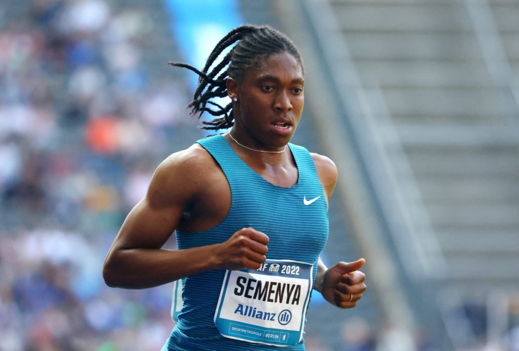 Women’s athletic runner competing in a track and field race, wearing a blue sports top with her name Semenya on race bib, running passionately during a competitive event in the stadium.