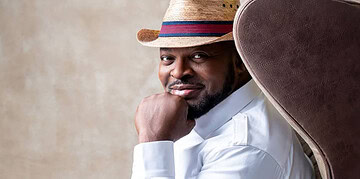 Stylish man wearing a straw hat and white shirt, sitting confidently on a modern chair, representing freelancing, creativity, and confidence in the workplace.