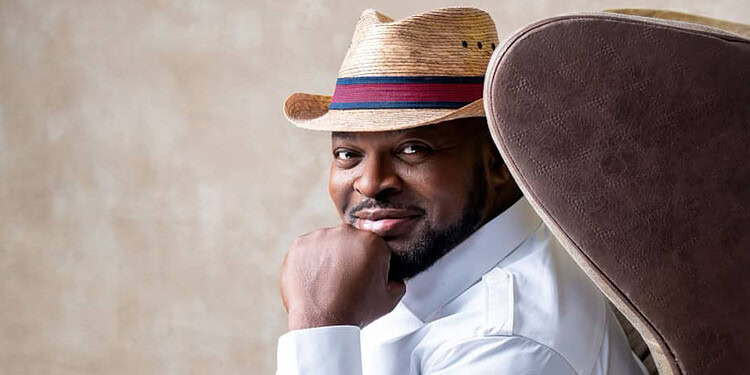 Stylish man wearing a straw hat and white shirt, sitting confidently on a modern chair, representing freelancing, creativity, and confidence in the workplace.