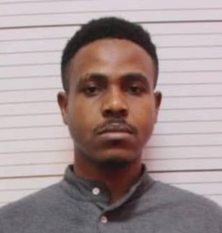 Young professional man with serious expression in casual attire, standing in front of a white wall, representing modern freelancing and remote work lifestyle, ideal for freelance news coverage.