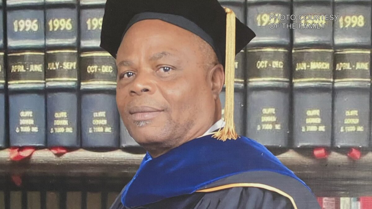 Man in academic gown and cap during graduation ceremony in front of bookshelf with legal books, celebrating academic achievement and success.