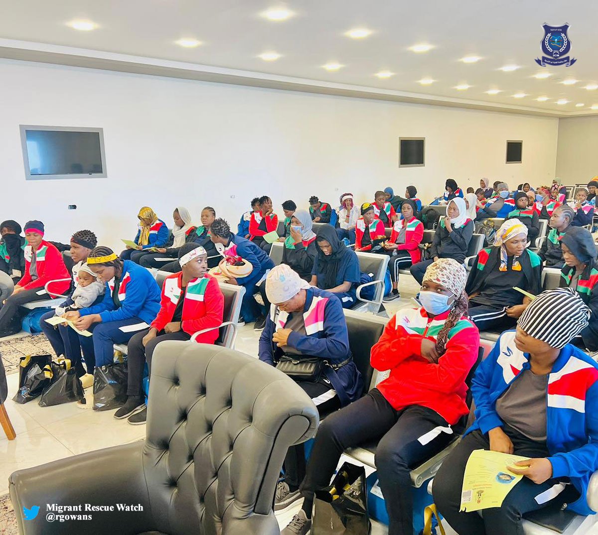 People attending a conference or seminar in a modern meeting room with white walls and multiple flat screen monitors.