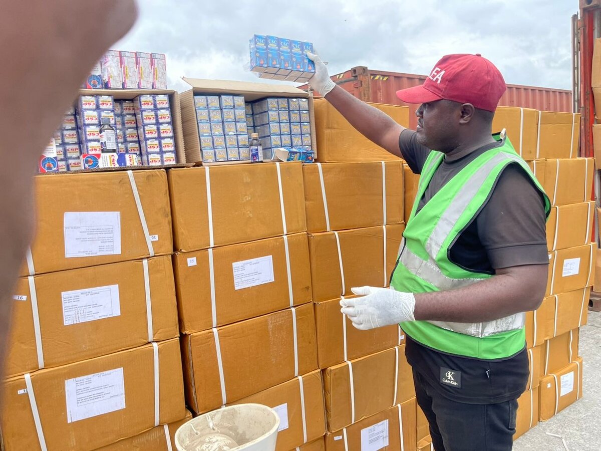 1. A worker in safety vest and red cap handling cargo and supplies at a busy shipping or distribution centre, highlighting logistics and supply chain operations in Africa.