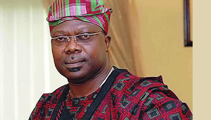 Man dressed in traditional Nigerian attire with a colorful hat, serious expression, in an indoor setting, representing Nigerian culture and heritage, likely at an official or cultural event.