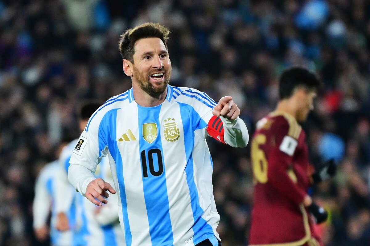 Argentina football player celebrating during a match, wearing national team jersey with captain armband, in a stadium filled with supporters, featuring iconic team badges and vibrant colours.