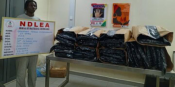 NDLDEA officer with seized drug packages and strategic command board, in a security or law enforcement environment.