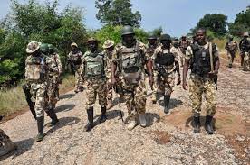 A group of soldiers in camouflage uniforms walking along a rural dirt road in a tactical operation.