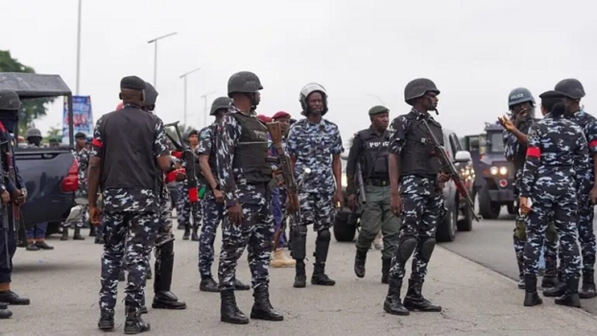 Uniformed police and military personnel gathered on a road, possibly for security or a public event, with vehicles in the background. The scene depicts law enforcement officers in tactical gear engaging in coordination or discussion.