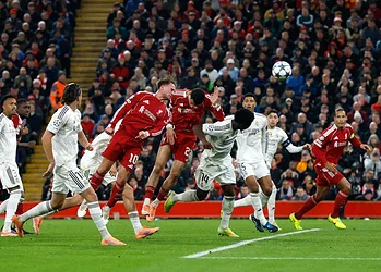 Vibrant soccer match between Real Madrid and Bayern Munich with players jumping to head the ball during a high-stakes Champions League game. Fans cheer in a packed stadium.