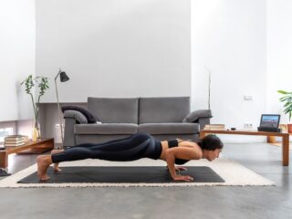 Fit woman practicing Chaturanga pose using online yoga training program in the tablet at home