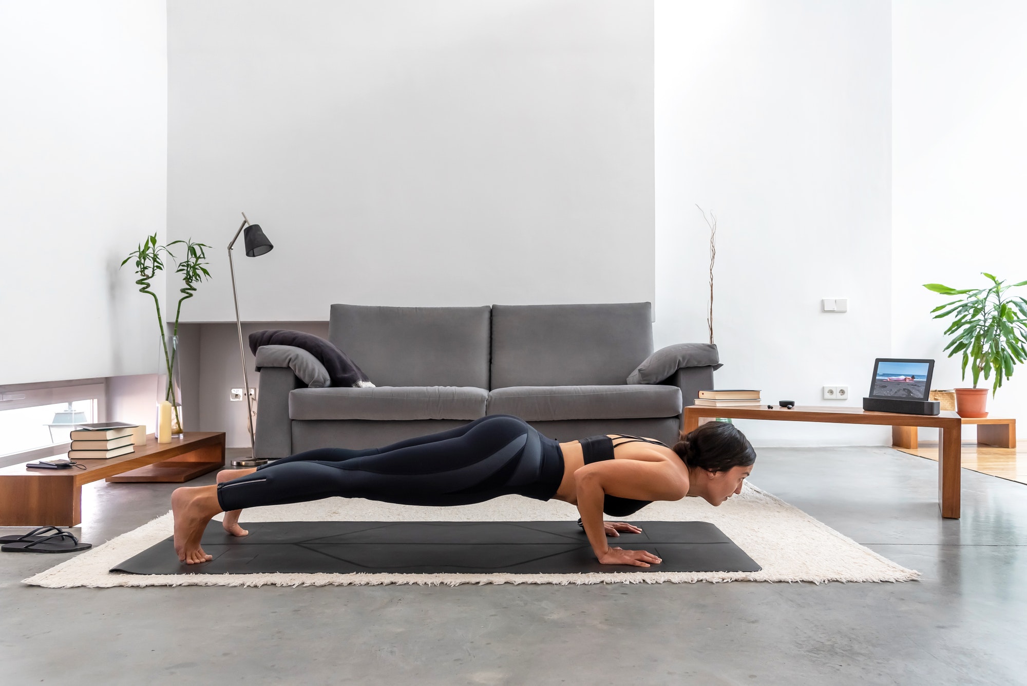 Fit woman practicing Chaturanga pose using online yoga training program in the tablet at home