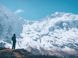 Woman on the mountain trail and looking on snow covered rocks