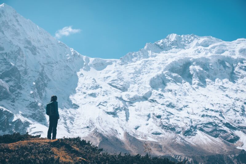 Woman on the mountain trail and looking on snow covered rocks