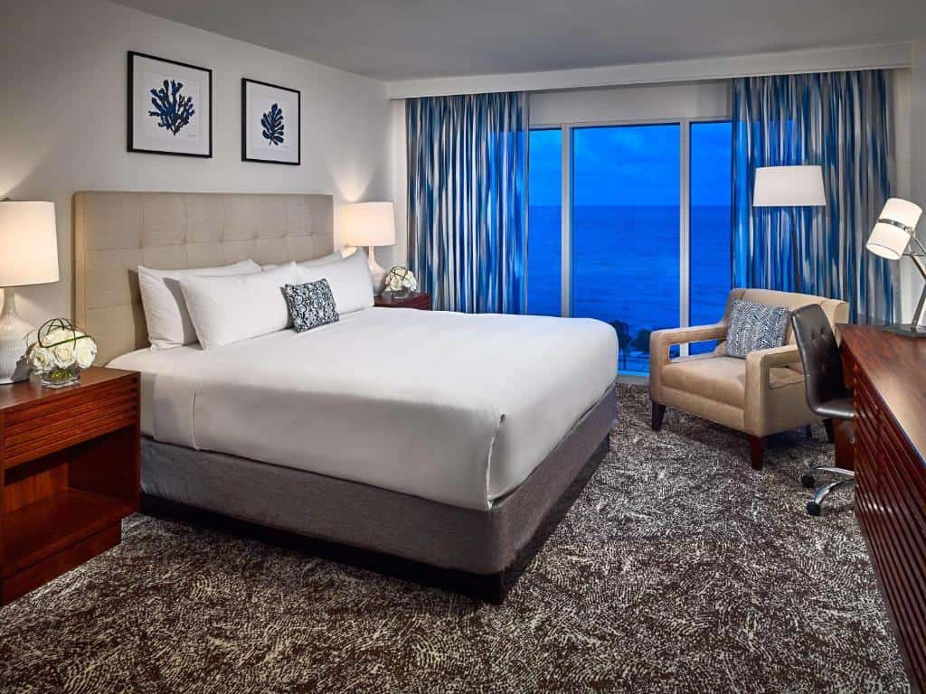 Hotel guestroom with a bed, seating area, and an ocean view.