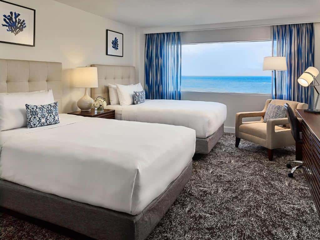 Hotel guestroom with two beds, seating area and an ocean view.