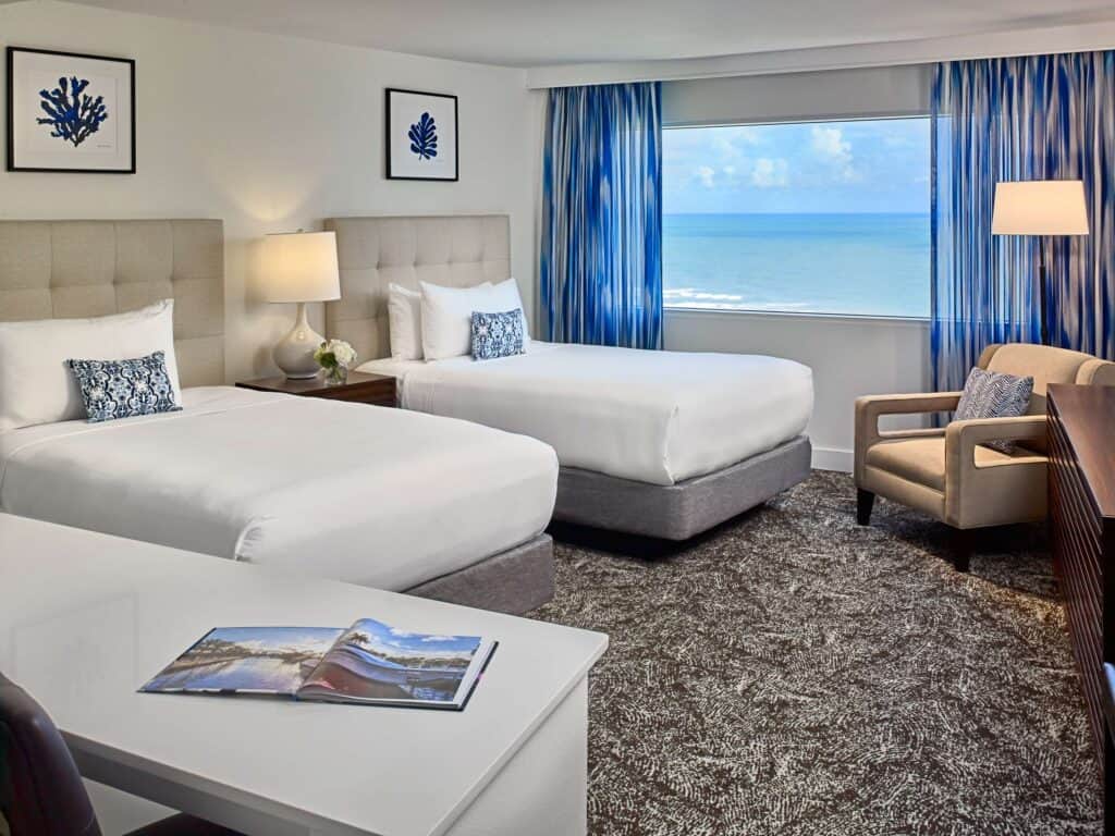 Hotel guestroom with two beds, working area, seating area, and an ocean view.