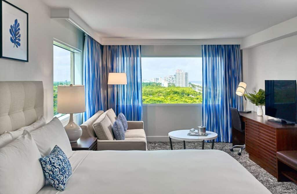 Hotel guestroom with a bed, seating area, and a beach view.