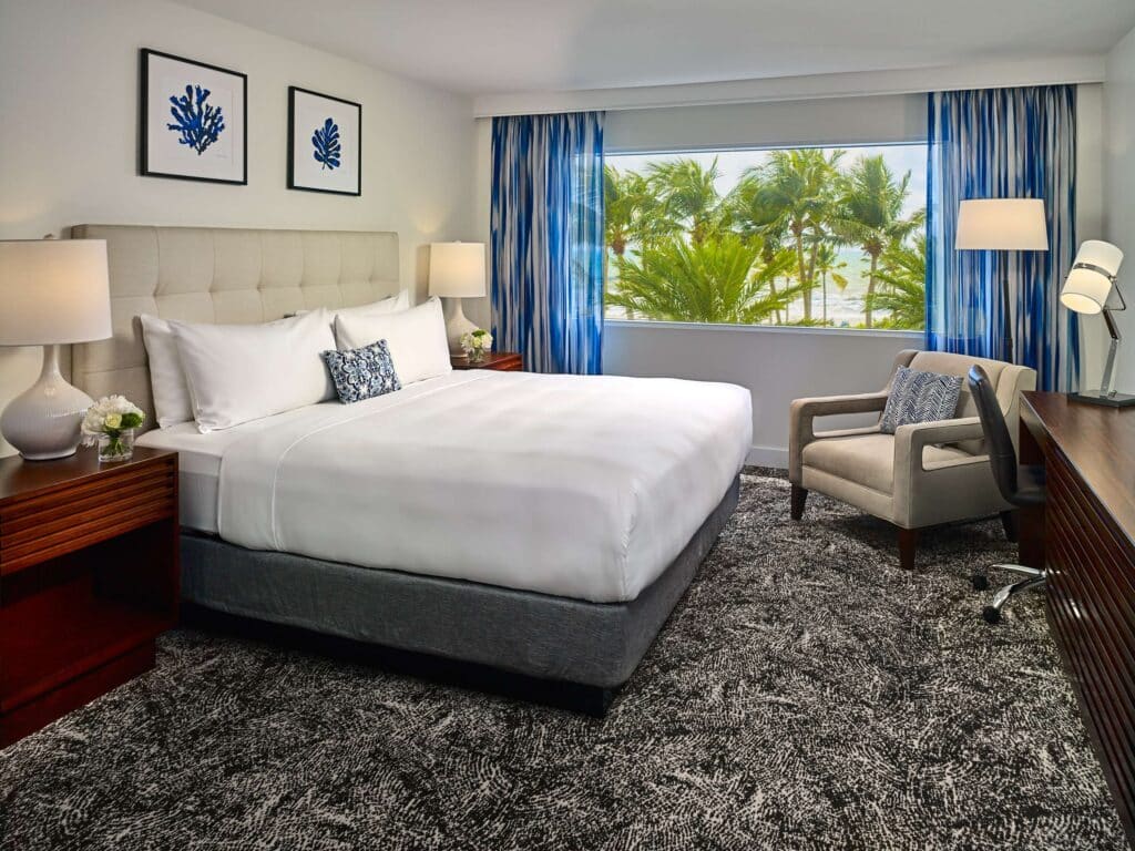 Hotel guestroom with a beach view, bed and a seating area.