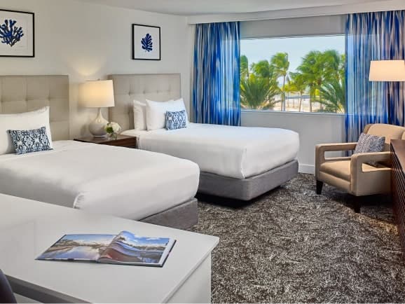 Hotel room with two beds, seating area, working desk, and a beach view.