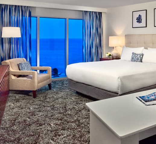 Hotel guestroom with a bed, working area, seating area, TV, and an ocean view.