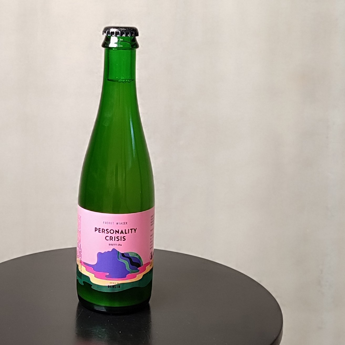 Craft beer bottle with colorful label, FUERST WIACEK Brewery, Personality Crisis Brett IPA, green glass, Berlin, innovative brewing, high-quality craft beer, modern brewery, unique beer flavors.