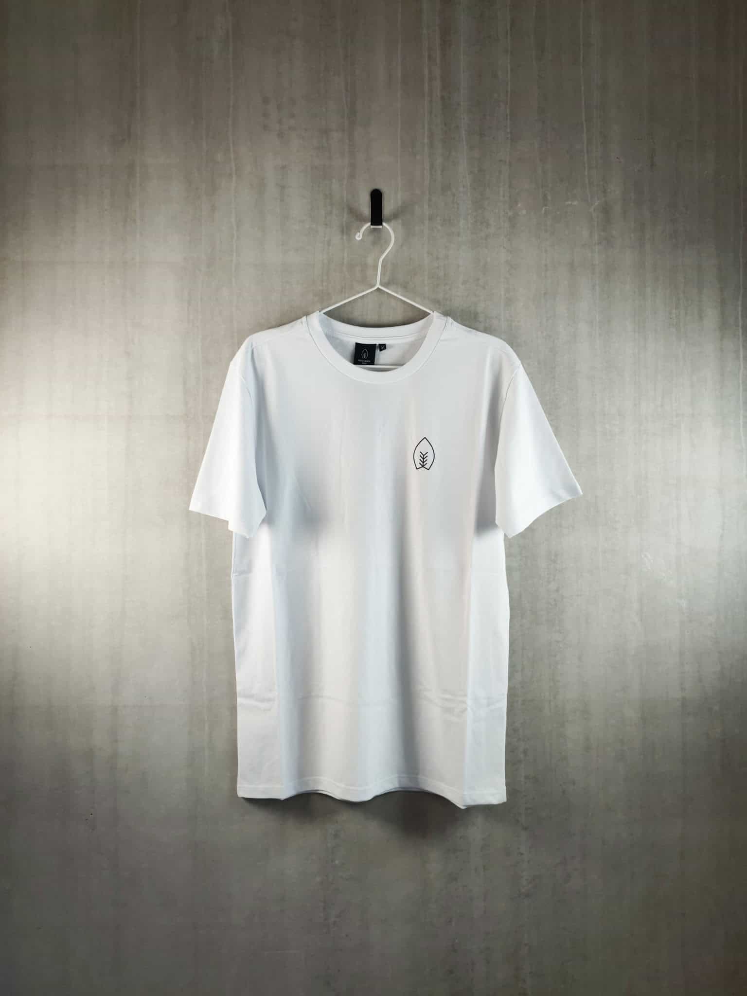 Weißes T-Shirt der Brauerei FUERST WIACEK mit minimalistischem Blatt-Logo, das an einem Haken an einer strukturierten Wand hängt und die moderne Craft-Bier-Mode und das Branding widerspiegelt.