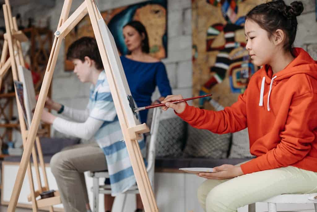 Children painting in an art class, guided by a teacher, fostering creativity and learning.
