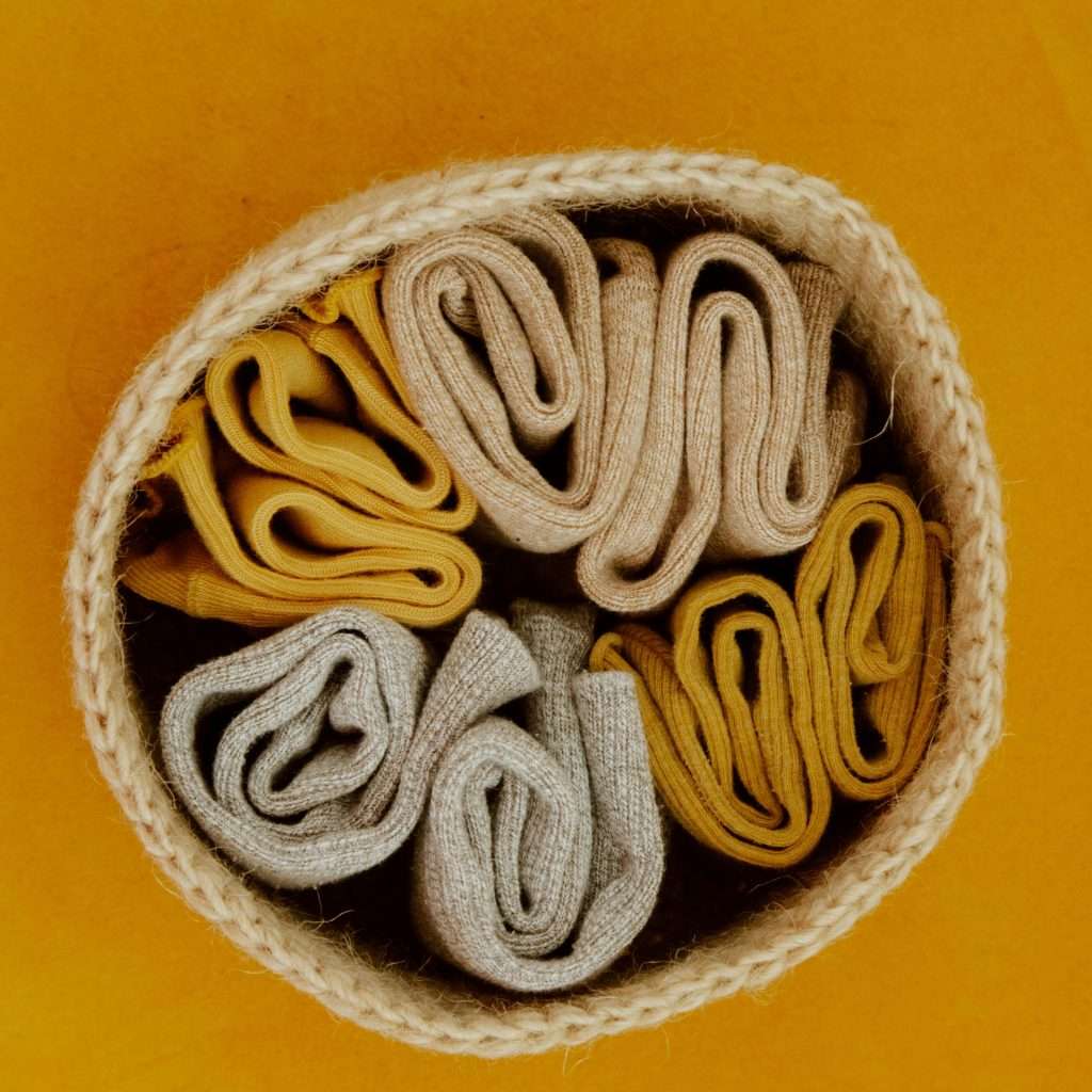 Top view of colorful rolled socks neatly arranged in a woven basket on an orange background.