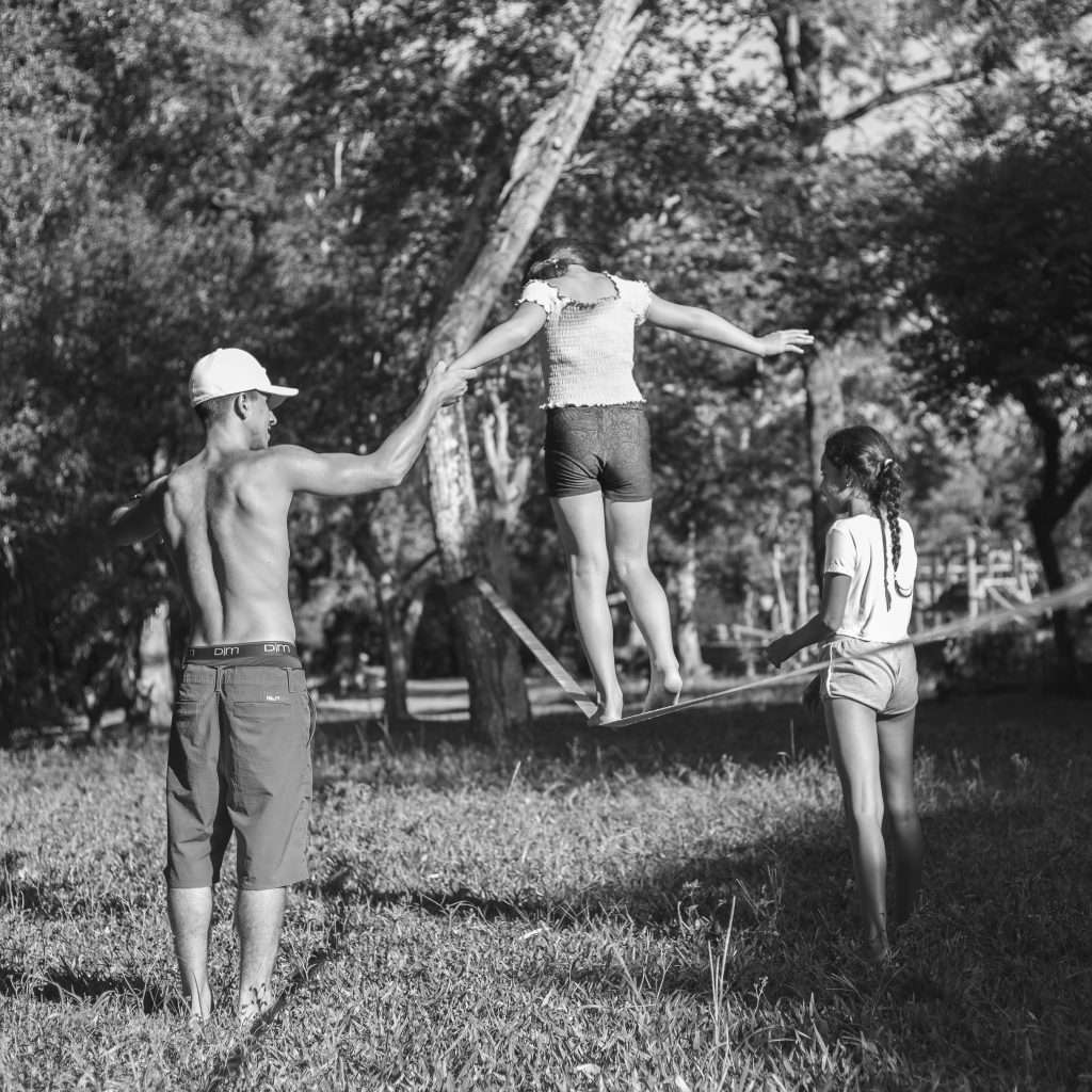 A man helping children practice slacklining in a wooded area.