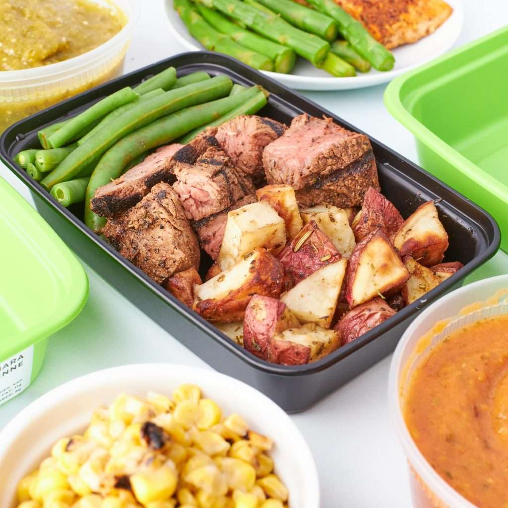 A vibrant meal prep container with grilled meat, green beans, and roasted potatoes.