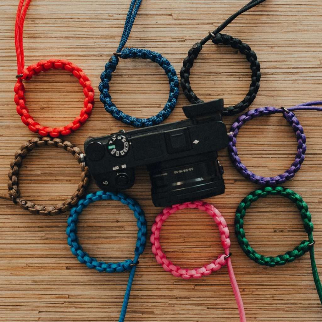 Colorful handmade bracelets arranged with a camera on a wooden surface.