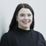 Lisa Krawczyk steht an eine Wand gelehnt und lächelt in die Kamera.