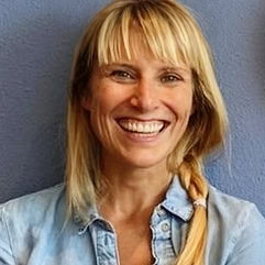 Sandra Schuster lacht in die Kamera. Sie hat blonde lange Haare, ein Pony und trägt eine Jeansjacke.