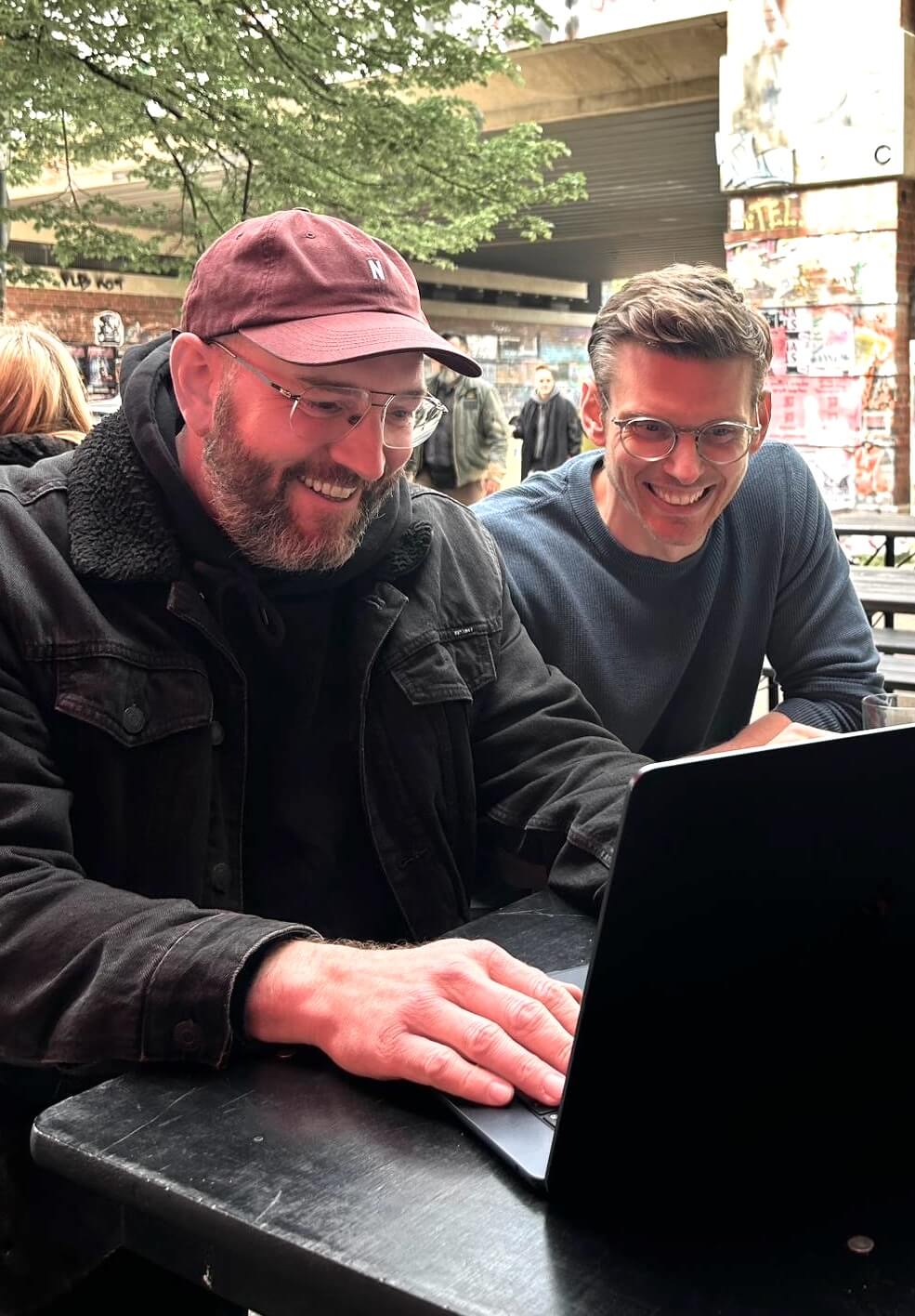Tobias & Johannes sitzen draußen vor einem Laptop und arbeiten zusammen an einer Webseite