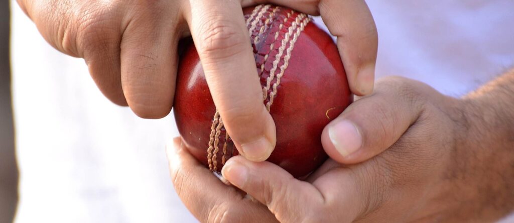 Red cricket ball with a white seam held by a person's hand, ready for play.