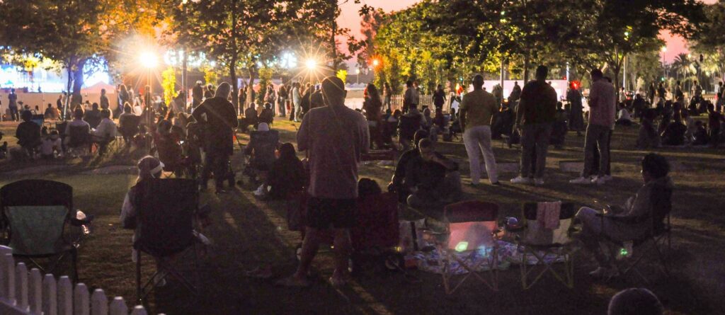Sunset outdoor gathering with people enjoying music and socialising in a park.
