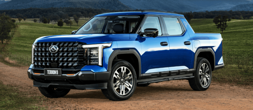 Blue Toyota Tundra pickup truck parked on grassy field with mountains in the background.