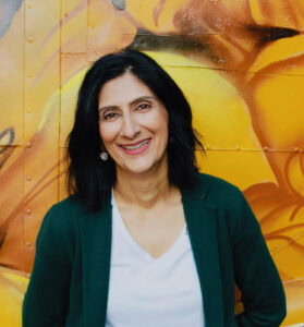 High-quality gemstone jewelry displayed by a smiling woman in front of a colorful graffiti wall.