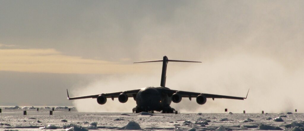 Aircraft landing on snow-covered runway in a winter landscape, with a cloudy sky.