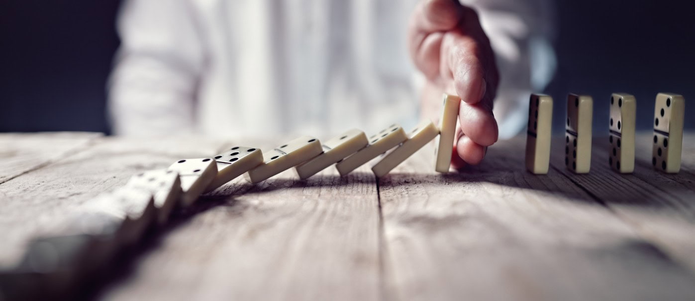 A domino being toppled to start a chain reaction on a wooden surface.