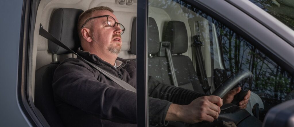 Sleepy man resting in car, possibly driver taking a nap during travel.